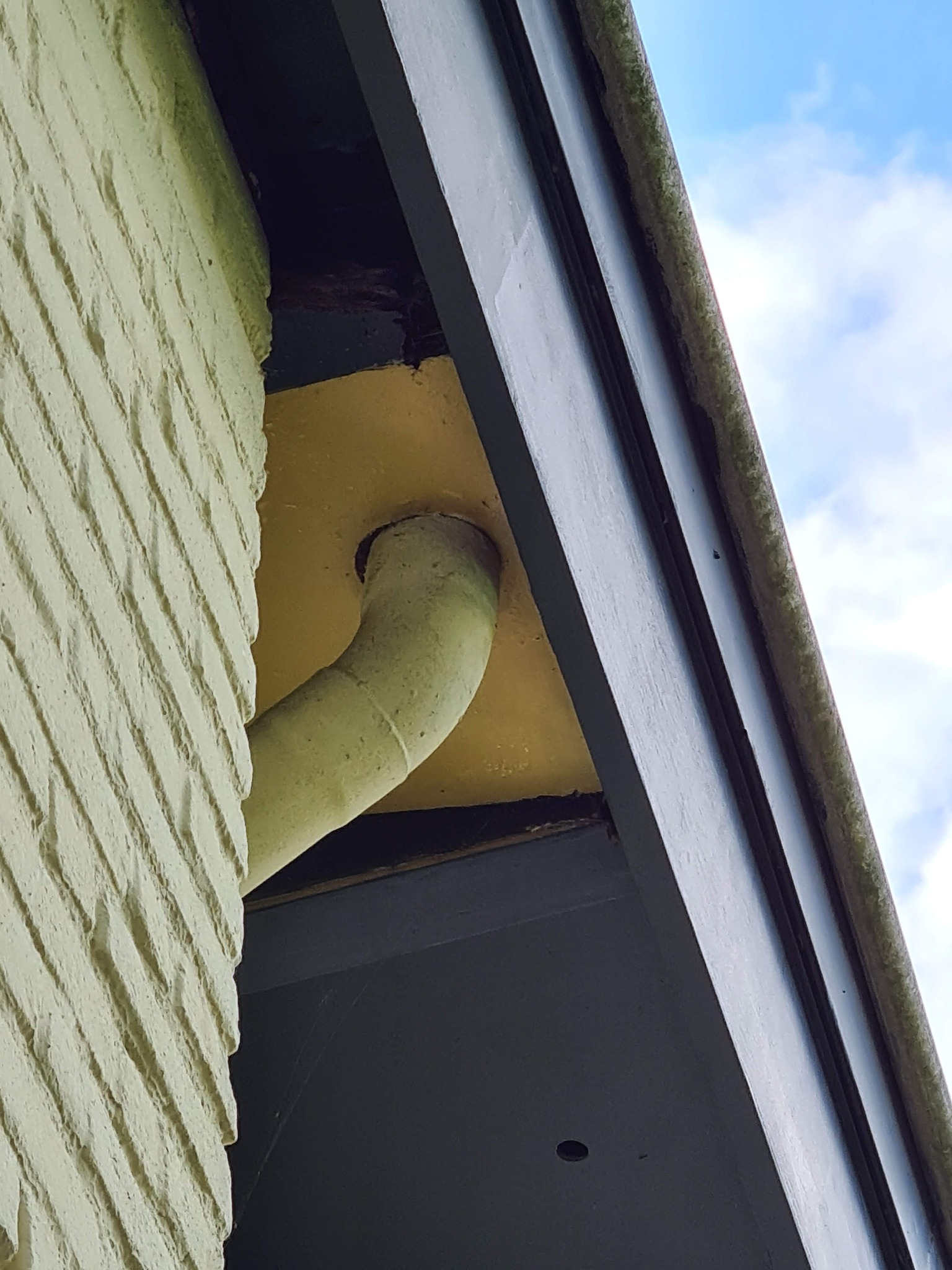 Fragment elewacji budynku z rynną, widoczne ślady zabrudzeń i mchu na elementach konstrukcyjnych.