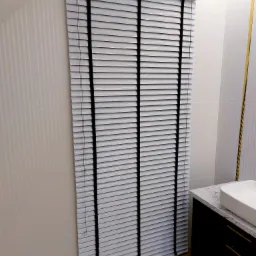 Białe żaluzje z czarnymi taśmami w łazience z marmurową umywalką, widoczne płytki ścienne z delikatnym wzorem i parkiet w jodełkę.