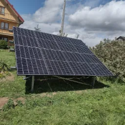 Panele słoneczne na metalowej konstrukcji ustawione na trawniku przed domem jednorodzinnym w słoneczny dzień.