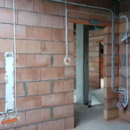 Wewnętrzne okablowanie elektryczne w surowym budynku z cegły, widoczne kable prowadzone w peszlach i puszki pod gniazdka, instalacja w trakcie realizacji.