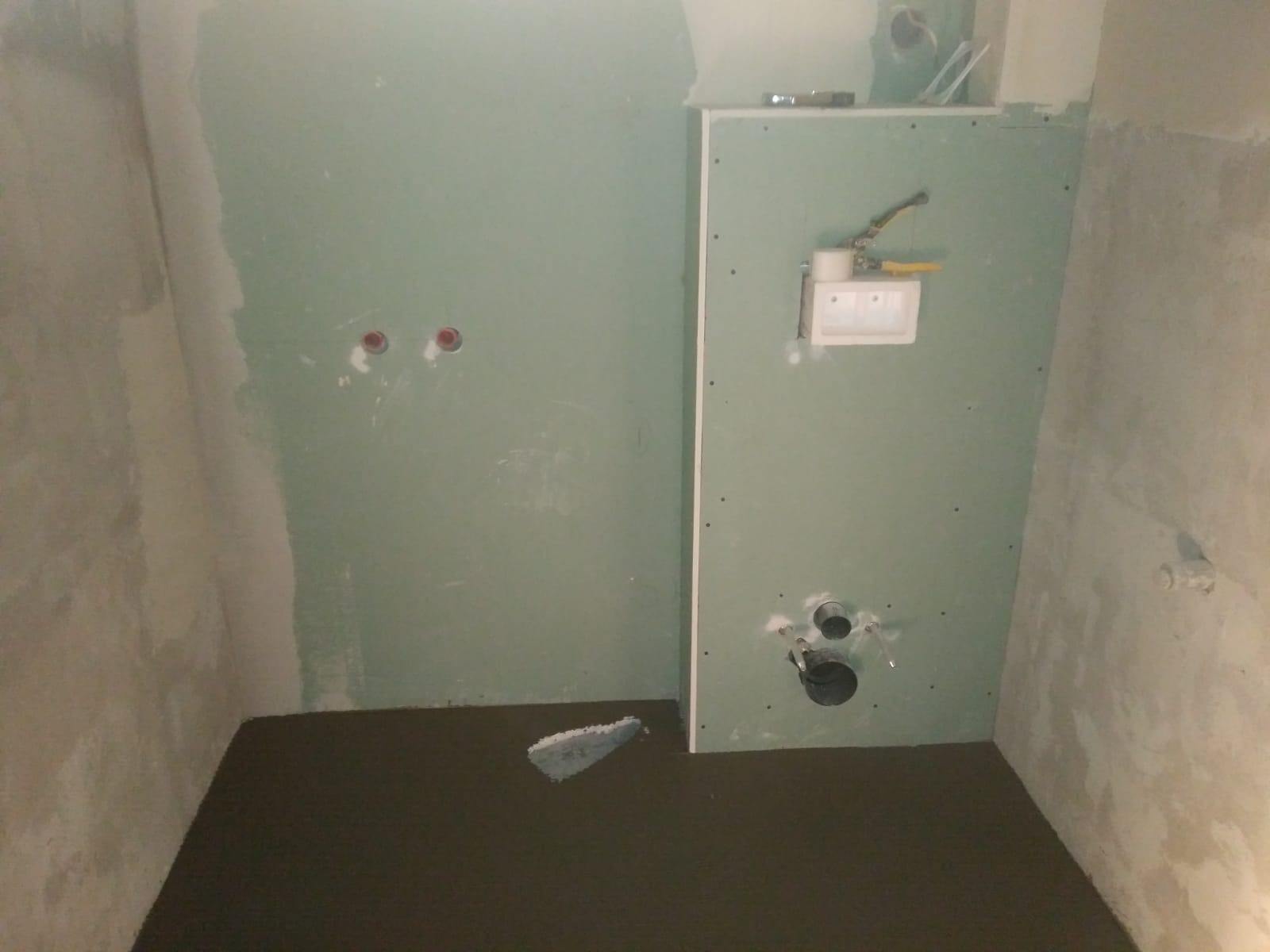 Przygotowanie do montażu podtynkowego stelaża WC z płytą kartonowo-gipsową, widoczne otwory na rury i instalacje, świeżo wylana wylewka na podłodze.