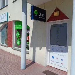 Fasada budynku z szyldem 'CUK Ubezpieczenia' nad wejściem, obok widoczne okno z napisem 'Tanie OC/AC 30 Towarzystw' oraz szyld 'Perfect Look Clinic'.