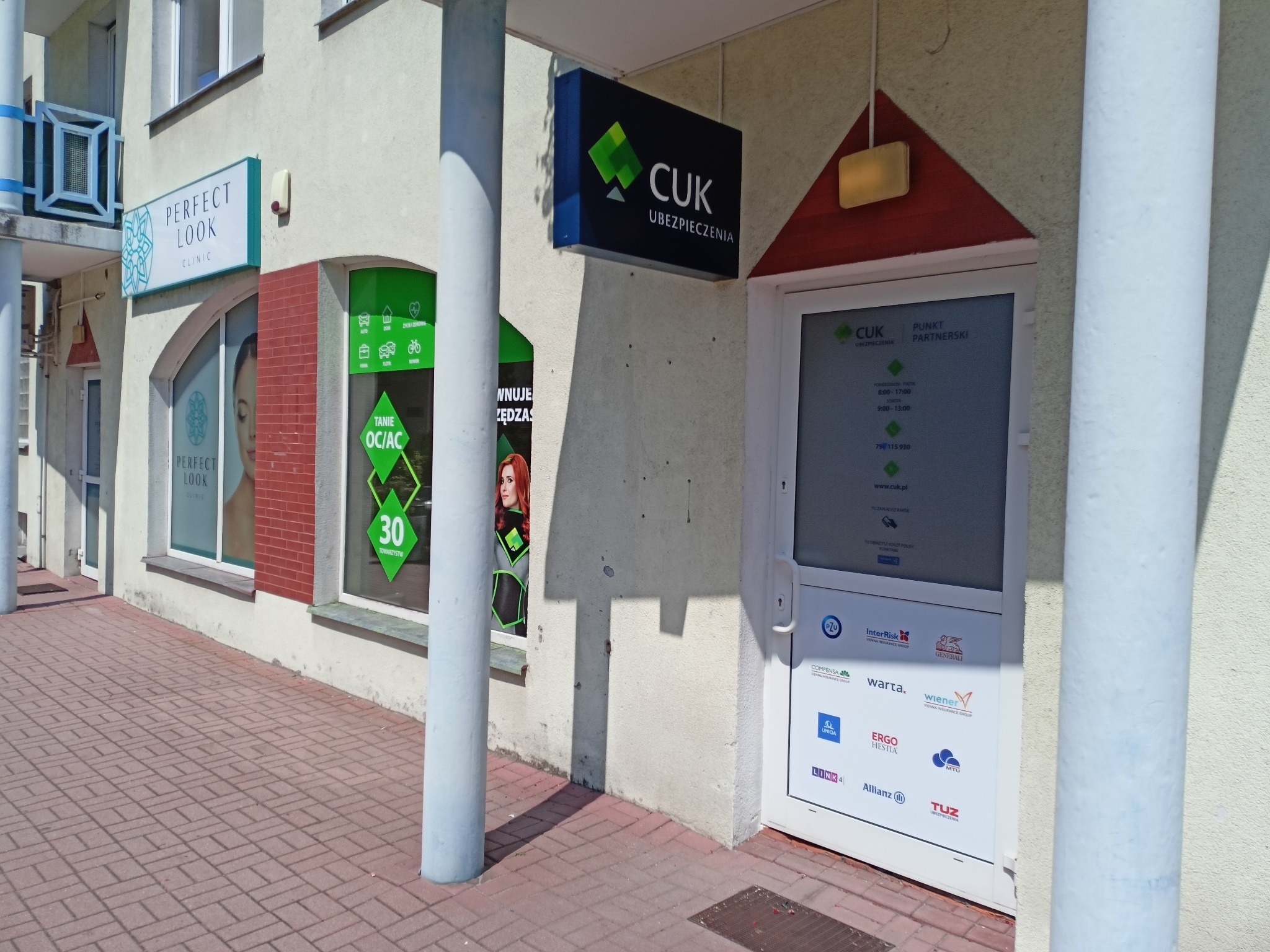 Fasada budynku z szyldem 'CUK Ubezpieczenia' nad wejściem, obok widoczne okno z napisem 'Tanie OC/AC 30 Towarzystw' oraz szyld 'Perfect Look Clinic'.