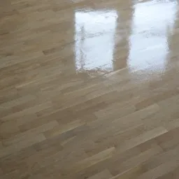 Błyszcząca, jasna drewniana podłoga parkietowa z widocznym odbiciem okna.