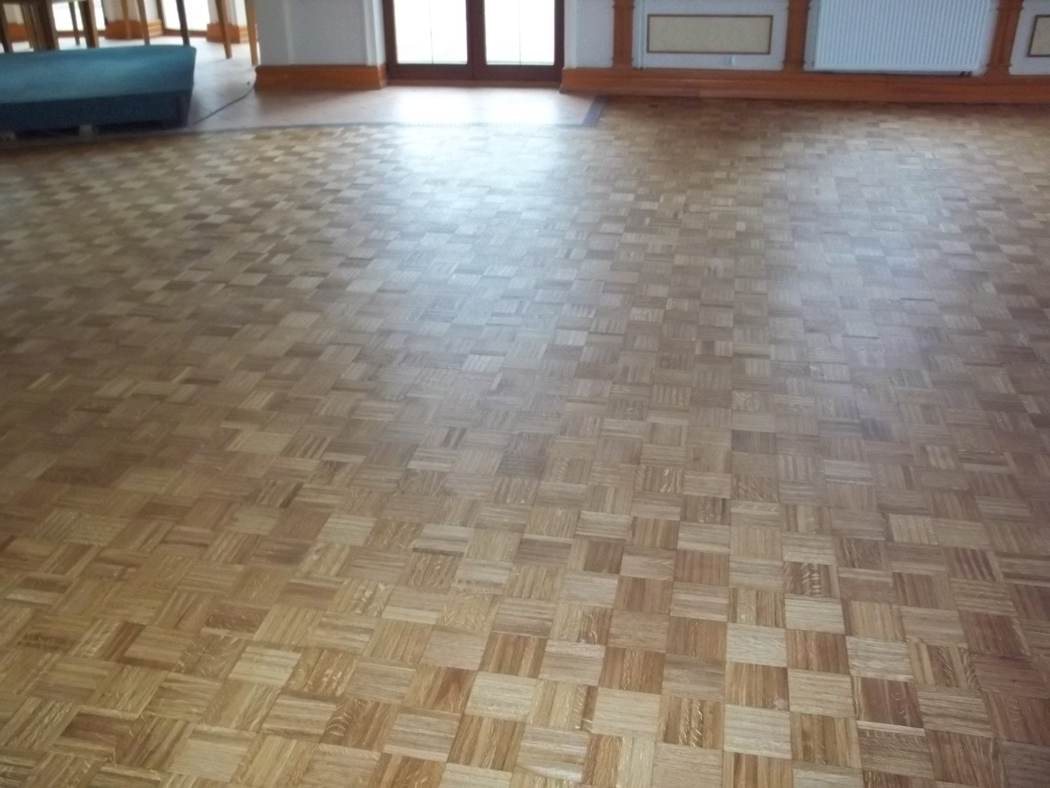 Ułożony parkiet w kwadraty w jasnym odcieniu drewna w przestronnym pomieszczeniu w Grajewie, widok na fragment podłogi z perspektywy.