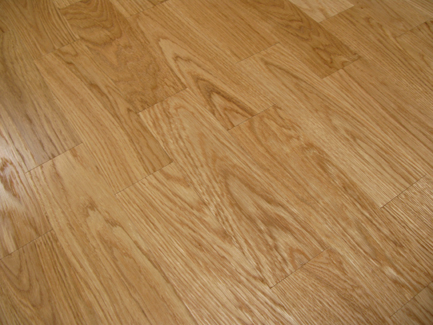 Jasnobrązowe panele podłogowe ułożone w jodełkę, widoczne subtelne łączenia między panelami i naturalny wzór drewna.