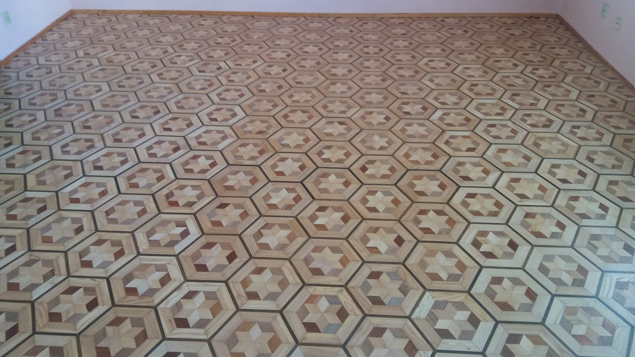 Parkiet ułożony w heksagonalny wzór z gwiazdą w centrum, wykonany z różnych odcieni drewna, widok z góry na wykończoną podłogę.