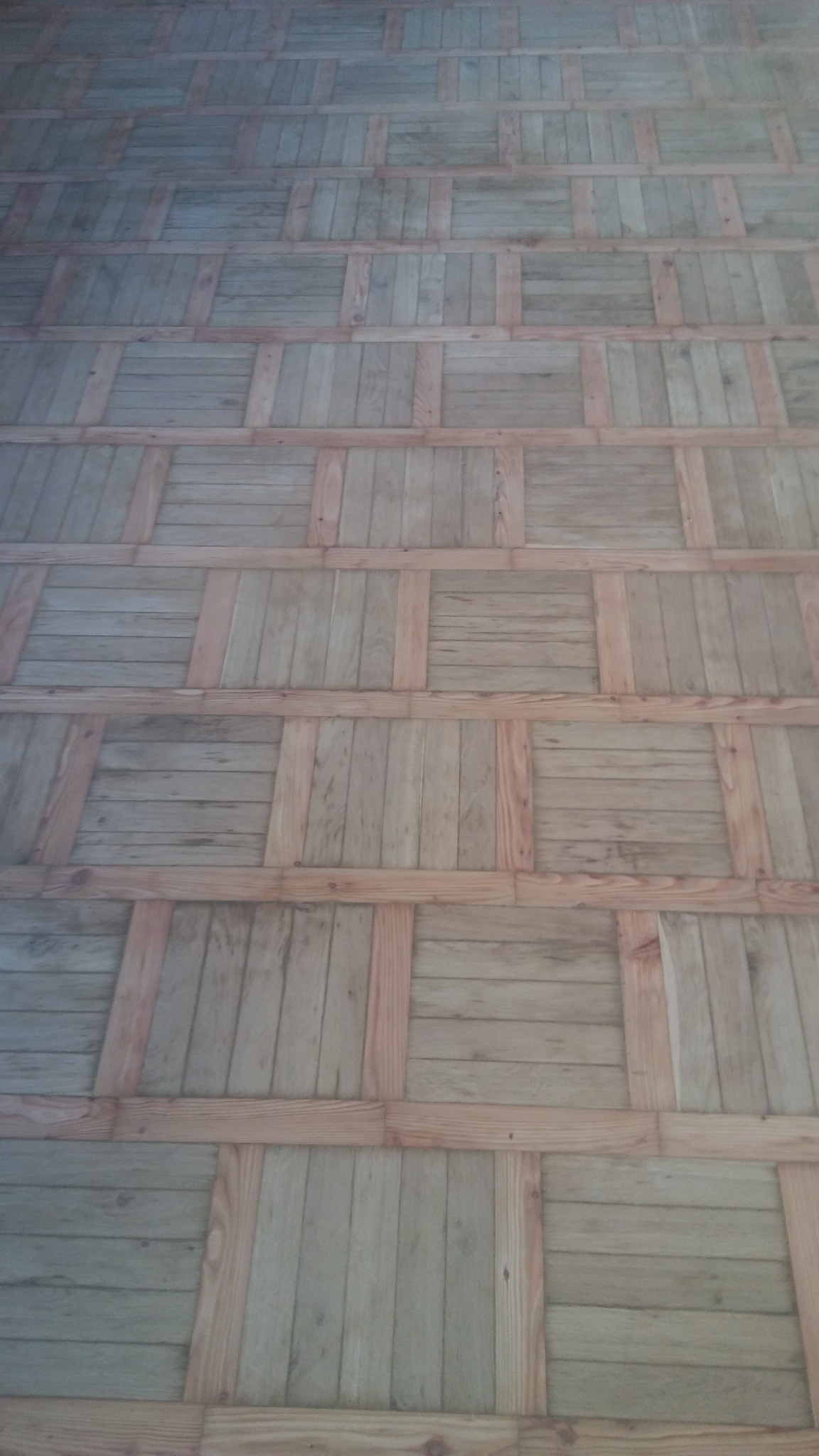 Ułożony parkiet w kwadraty z jasnego drewna, widoczne słoje i naturalna kolorystyka, wzór szachownicy.