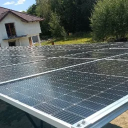 Instalacja paneli słonecznych na konstrukcji naziemnej przed domem jednorodzinnym, widok na panele z perspektywy niskiego kąta.