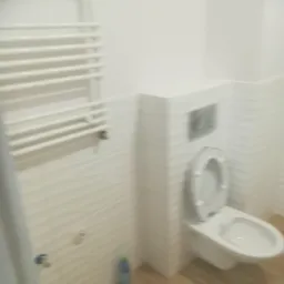 Wykończona łazienka z białą toaletą, grzejnikiem drabinkowym i dekoracyjnymi płytkami ściennymi z subtelnym wzorem fal.