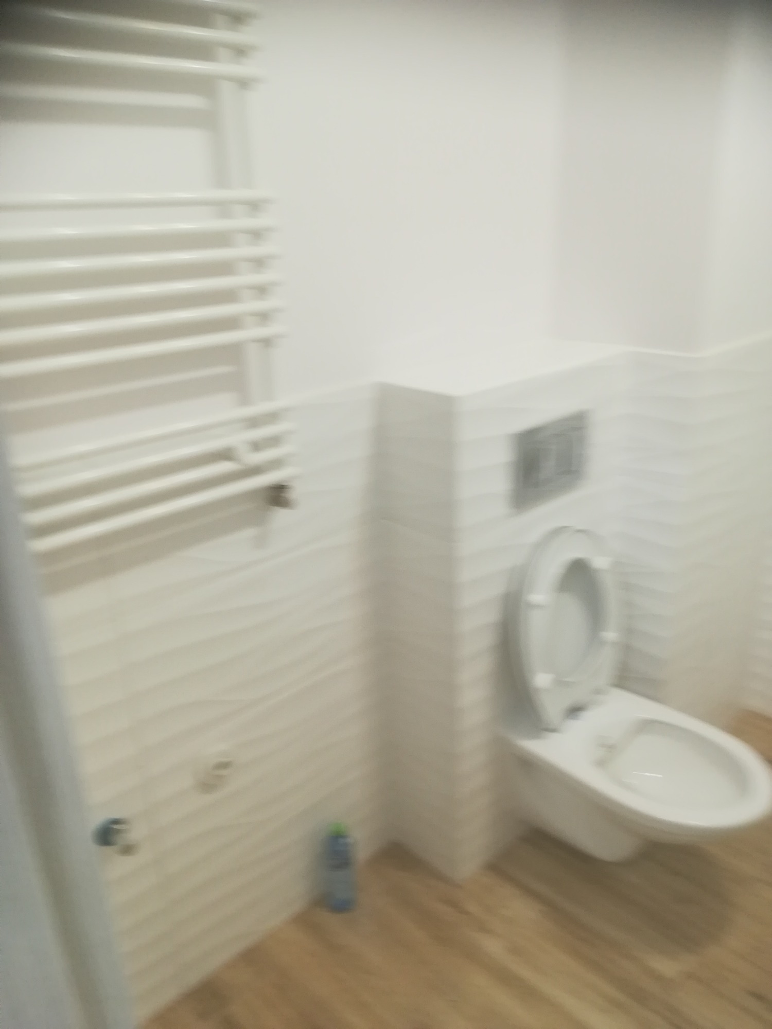 Wykończona łazienka z białą toaletą, grzejnikiem drabinkowym i dekoracyjnymi płytkami ściennymi z subtelnym wzorem fal.