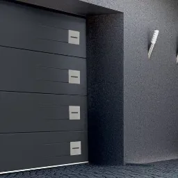 Nowoczesna, antracytowa brama garażowa segmentowa z poziomymi przetłoczeniami i kwadratowymi, metalowymi akcentami, obok dopasowane kolorystycznie drzwi wejściowe z długim, pionowym uchwytem...