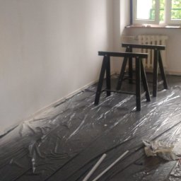 PaqoTech - Przygotowane do malowania pomieszczenie z zabezpieczoną folią podłogą, dwoma kozłami malarskimi i wałkami do malowania w folii.