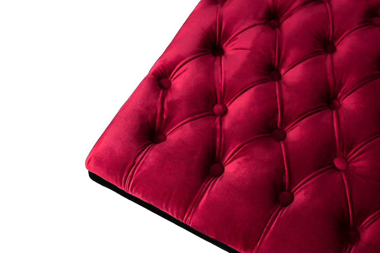 Fragment bordowego, pikowanego pufa z aksamitną tapicerką, widoczny z bliska pod kątem.