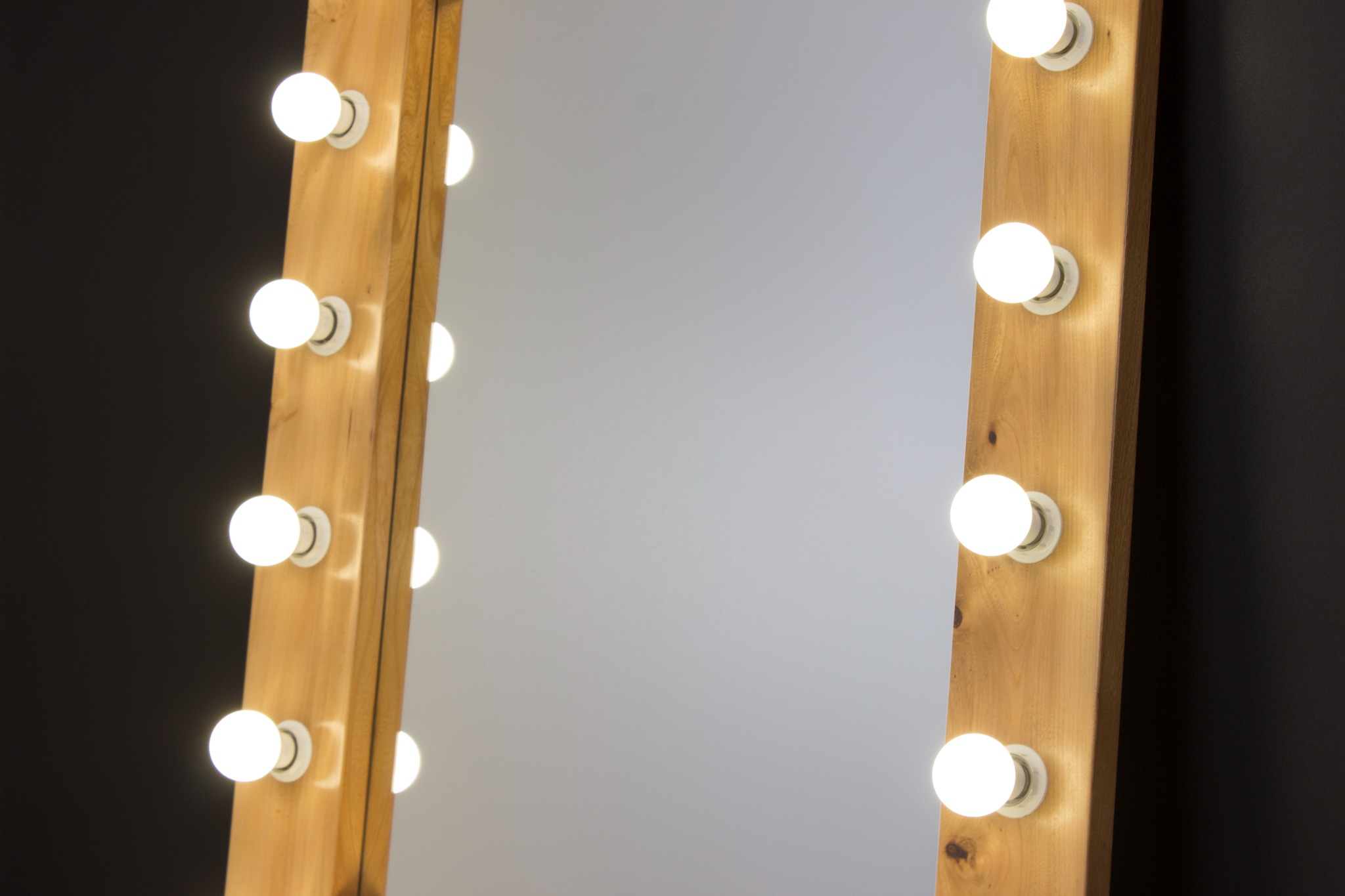 Drewniane lustro w stylu Hollywood z żarówkami po bokach, ustawione na tle ciemnej ściany.