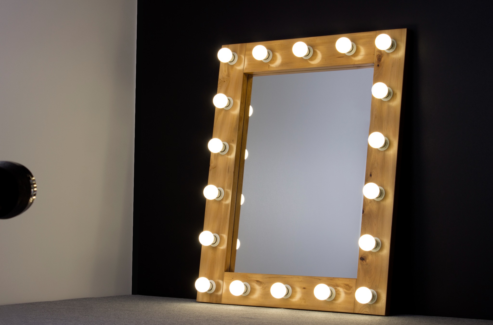 Drewniane lustro do makijażu z żarówkami w studio, oświetlone z boku dodatkowym reflektorem.