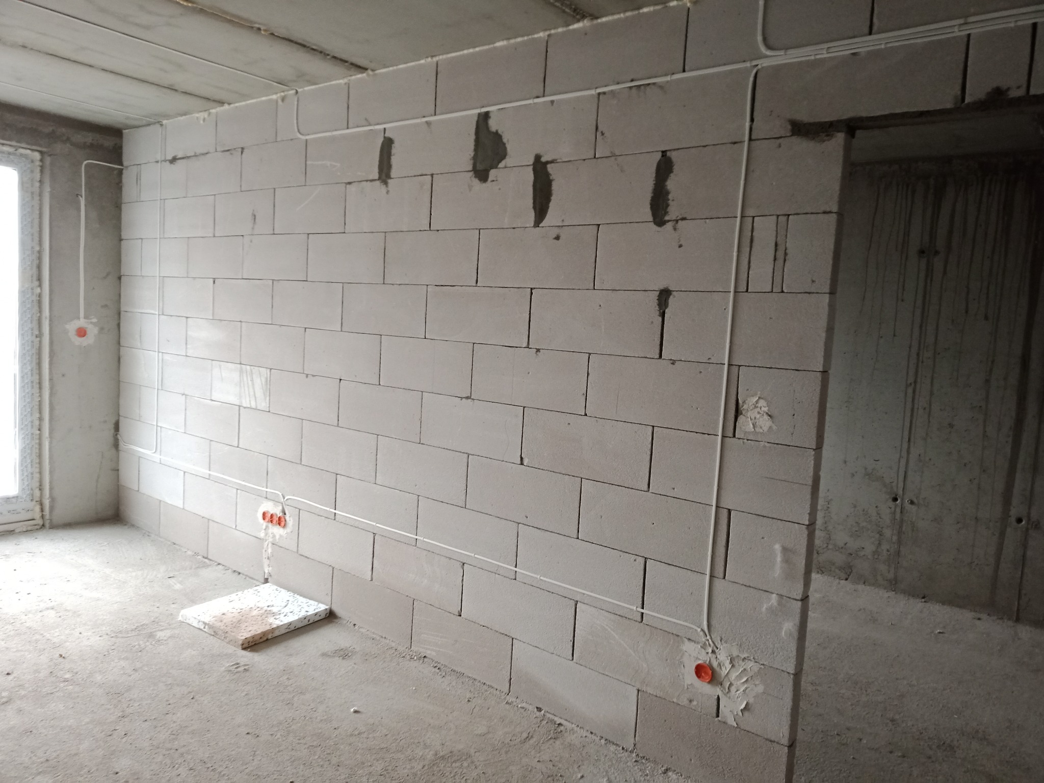 Surowy stan: białe przewody elektryczne poprowadzone po ścianie z betonu komórkowego w nowym budynku, widoczne puszki instalacyjne i ślady po zaprawie.