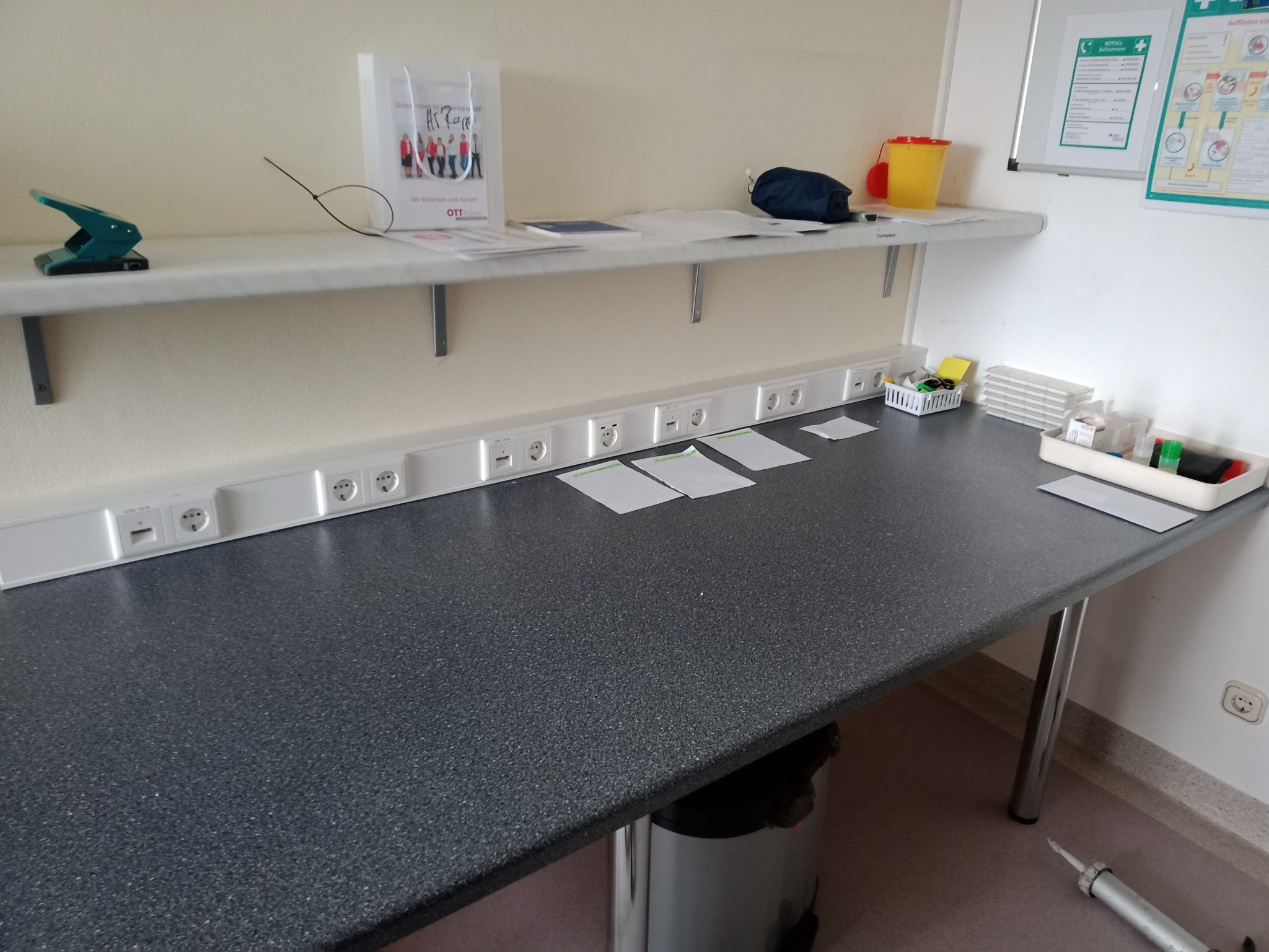 Rząd gniazdek elektrycznych i gniazd sieciowych zamontowanych na ścianie w Trzebiatowie, widoczne także elementy biurowe na blacie i półce.