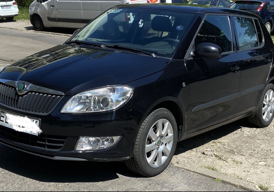 Czarny samochód Skoda Fabia hatchback zaparkowany na chodniku, widok z przodu, z widocznymi srebrnymi felgami i odblaskami na karoserii.