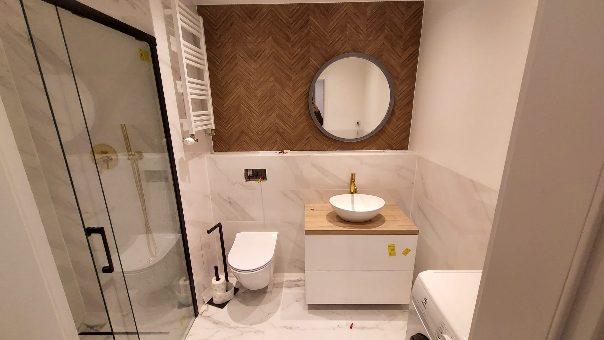 Nowoczesna łazienka z kabiną prysznicową typu walk-in, umywalką nablatową na drewnianym blacie, toaletą podwieszaną i dekoracyjną ścianą z drewnopodobnych płytek ułożonych w jodełkę.