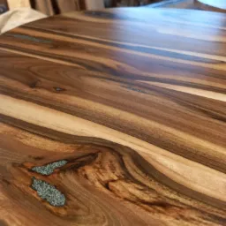 Szczegółowe ujęcie polerowanego, okrągłego blatu z egzotycznego drewna z żywiczną inkrustacją, ukazujące unikalny układ słojów i fakturę.