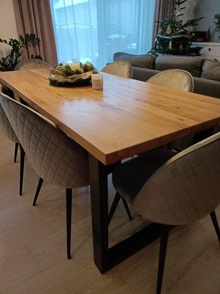 Stół z blatem z jasnego drewna na czarnych, metalowych nogach w nowoczesnym wnętrzu z krzesłami tapicerowanymi w kolorze szarym i świąteczną dekoracją.