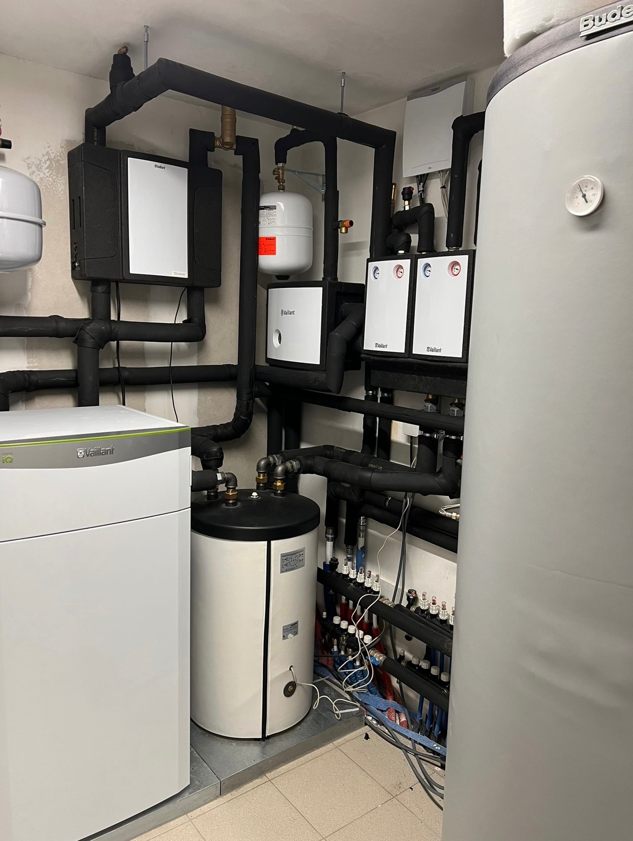 Kotłownia z zainstalowanym piecem gazowym, zbiornikiem buforowym, rozdzielaczem i czarnymi rurami izolowanymi termicznie.