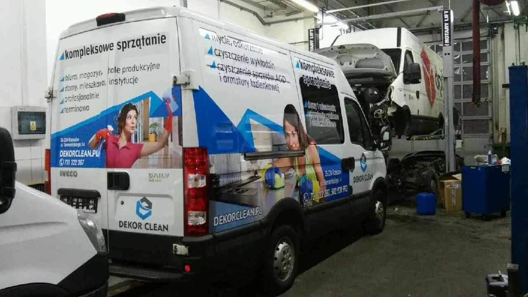 Samochód dostawczy firmy sprzątającej Dekor Clean z reklamą usług kompleksowego sprzątania biur, magazynów, hal produkcyjnych, domów, mieszkań i instytucji, zaparkowany w warsztacie samochodowym...
