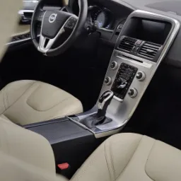 Wnętrze samochodu Volvo XC60 z jasną, skórzaną tapicerką, widok na deskę rozdzielczą, kierownicę z logo Volvo i automatyczną skrzynię biegów.