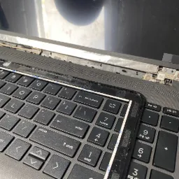 Rozłożony laptop z odpiętą ramką klawiatury, widoczne elementy mocujące ekran i klawisze, naprawa w toku.