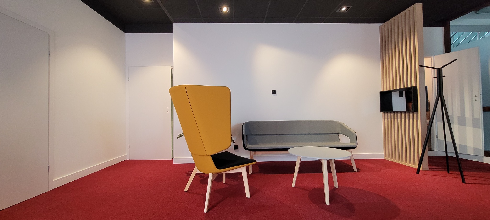 Nowoczesne wnętrze biurowe w Jeleniej Górze z żółtym fotelem, szarą sofą i stolikiem na czerwonej wykładzinie dywanowej, oświetlone punktowymi lampami.