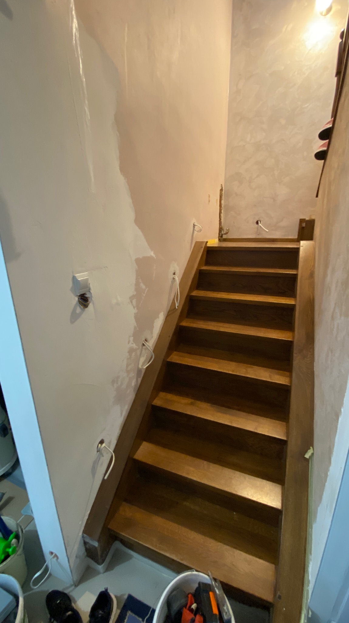 Drewniane schody w trakcie montażu, z widocznymi przewodami elektrycznymi wystającymi ze ściany, przygotowywanej do wykończenia.