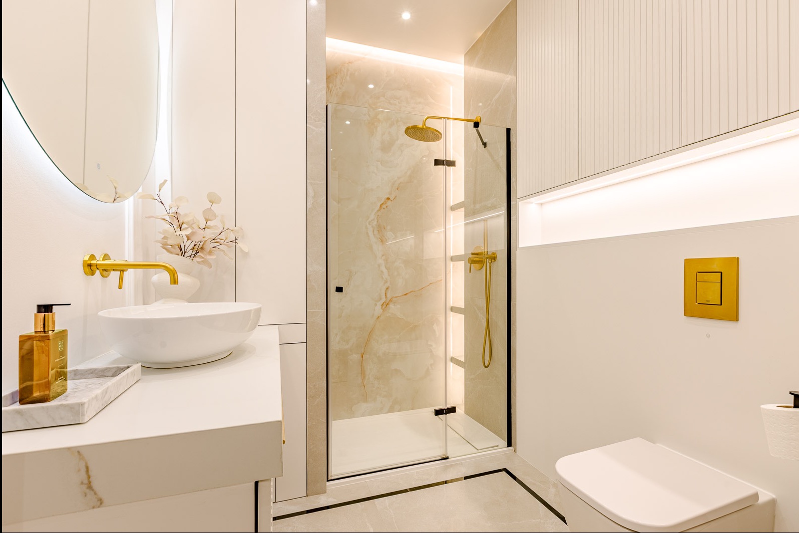 Elegancka łazienka z kabiną prysznicową, umywalką nablatową i złotymi akcentami. Minimalistyczny design, jasne kolory i subtelne oświetlenie LED.