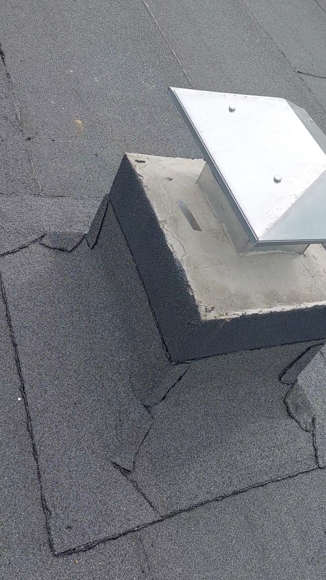 Szczegółowe ujęcie płaskiego dachu pokrytego papą bitumiczną wokół komina, z widocznymi łączeniami i obróbkami.