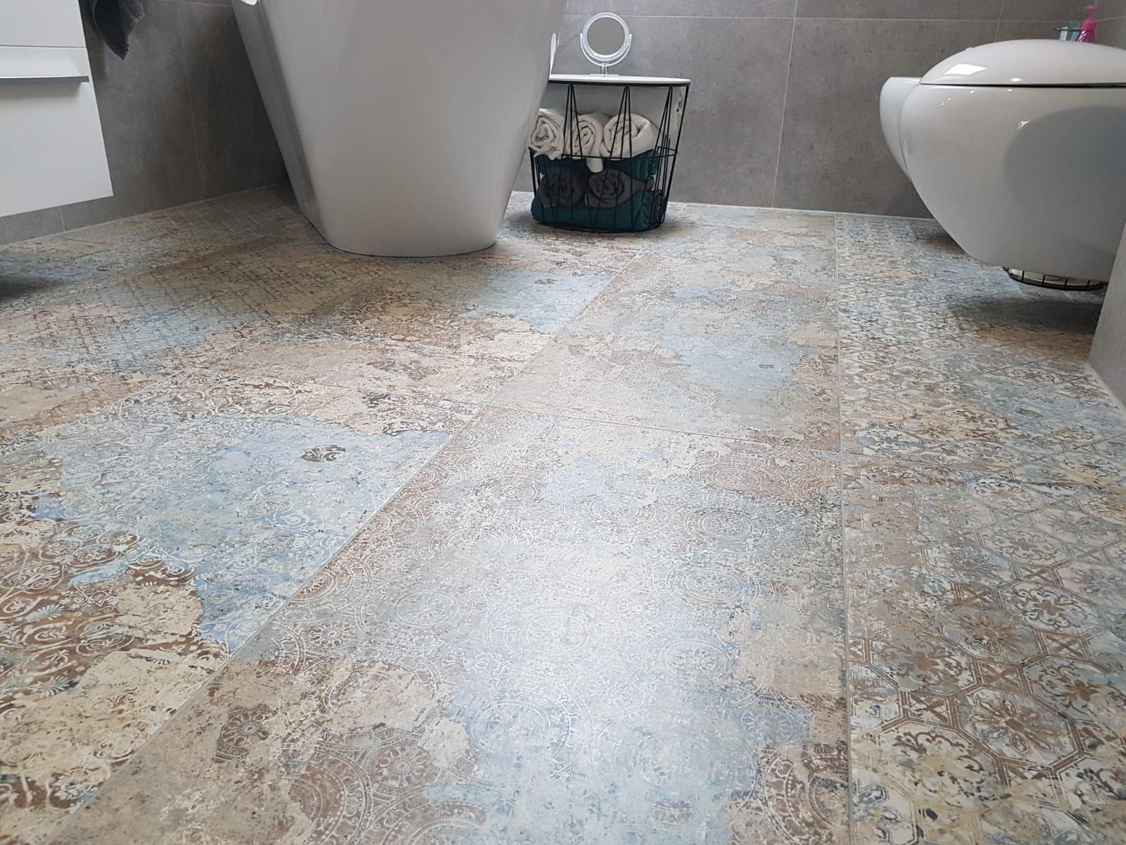 Ułożone płytki podłogowe w łazience z wzorem vintage, widoczne elementy wyposażenia: toaleta i koszyk na ręczniki.