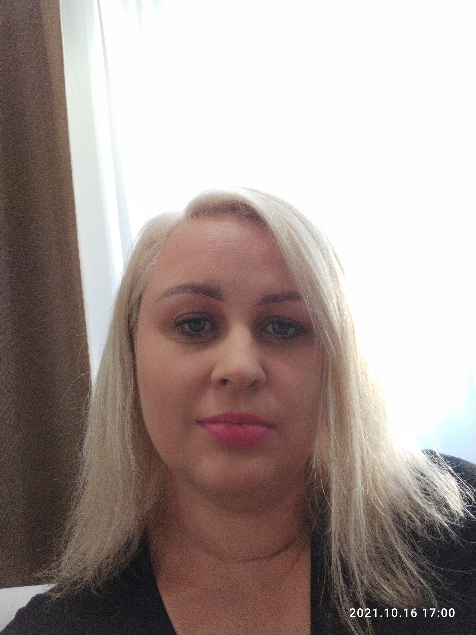 Portret kobiety z blond włosami i różowymi ustami, sfotografowanej z dołu, z widoczną datą 2021.10.16 17:00 w prawym dolnym rogu.