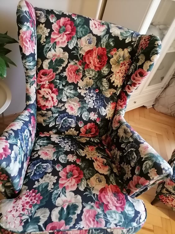 Fotel uszak z ciemną tapicerką w kwiaty, widoczny na tle parkietu i białej komody w Bydgoszczy.