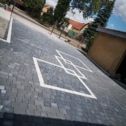 Ułożona kostka brukowa w odcieniach szarości z białym wzorem geometrycznym na podjeździe, widok z góry pod kątem.