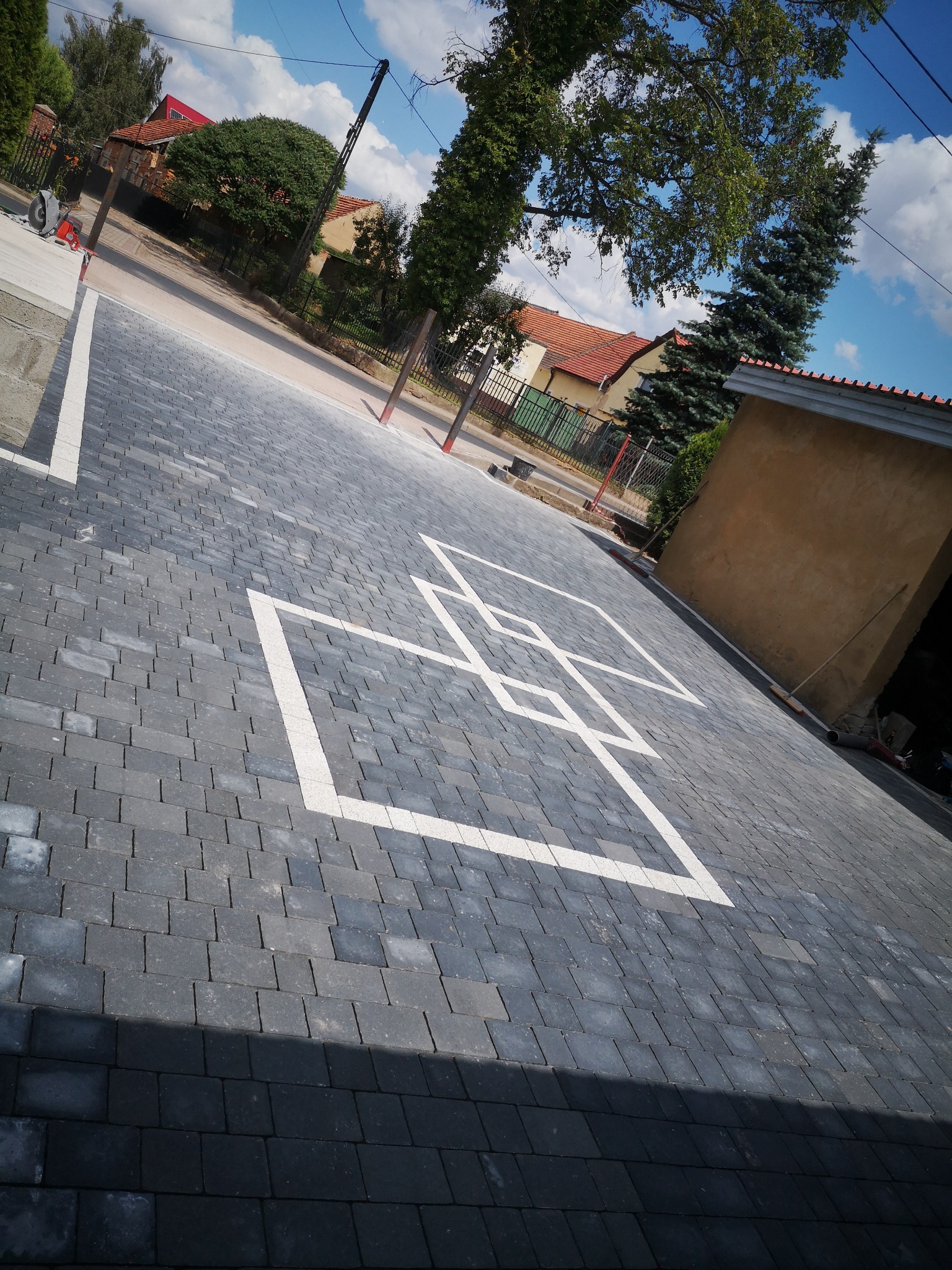 Ułożona kostka brukowa w odcieniach szarości z białym wzorem geometrycznym na podjeździe, widok z góry pod kątem.