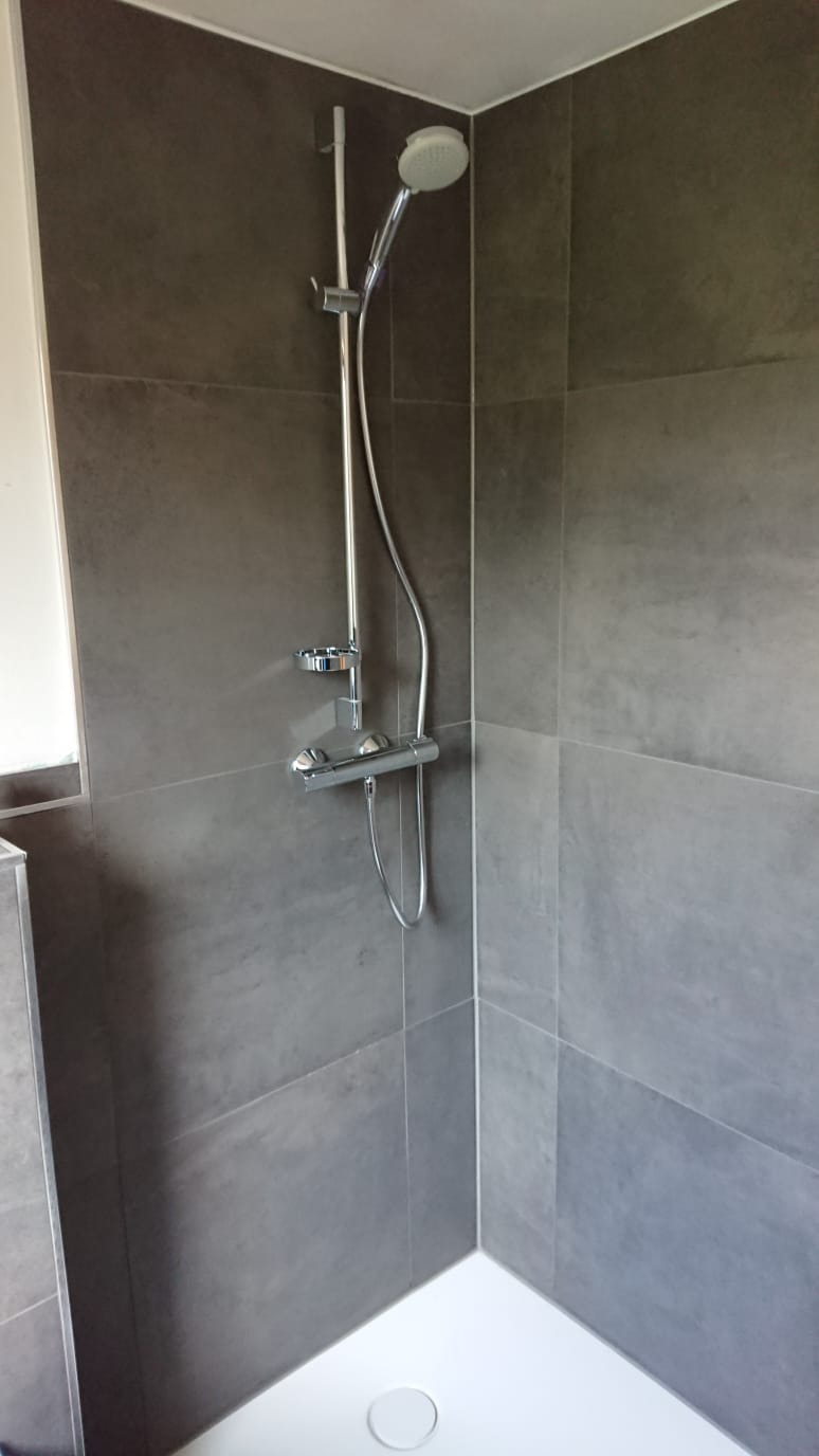 Nowoczesna kabina prysznicowa z szarymi płytkami wielkoformatowymi i chromowaną armaturą.