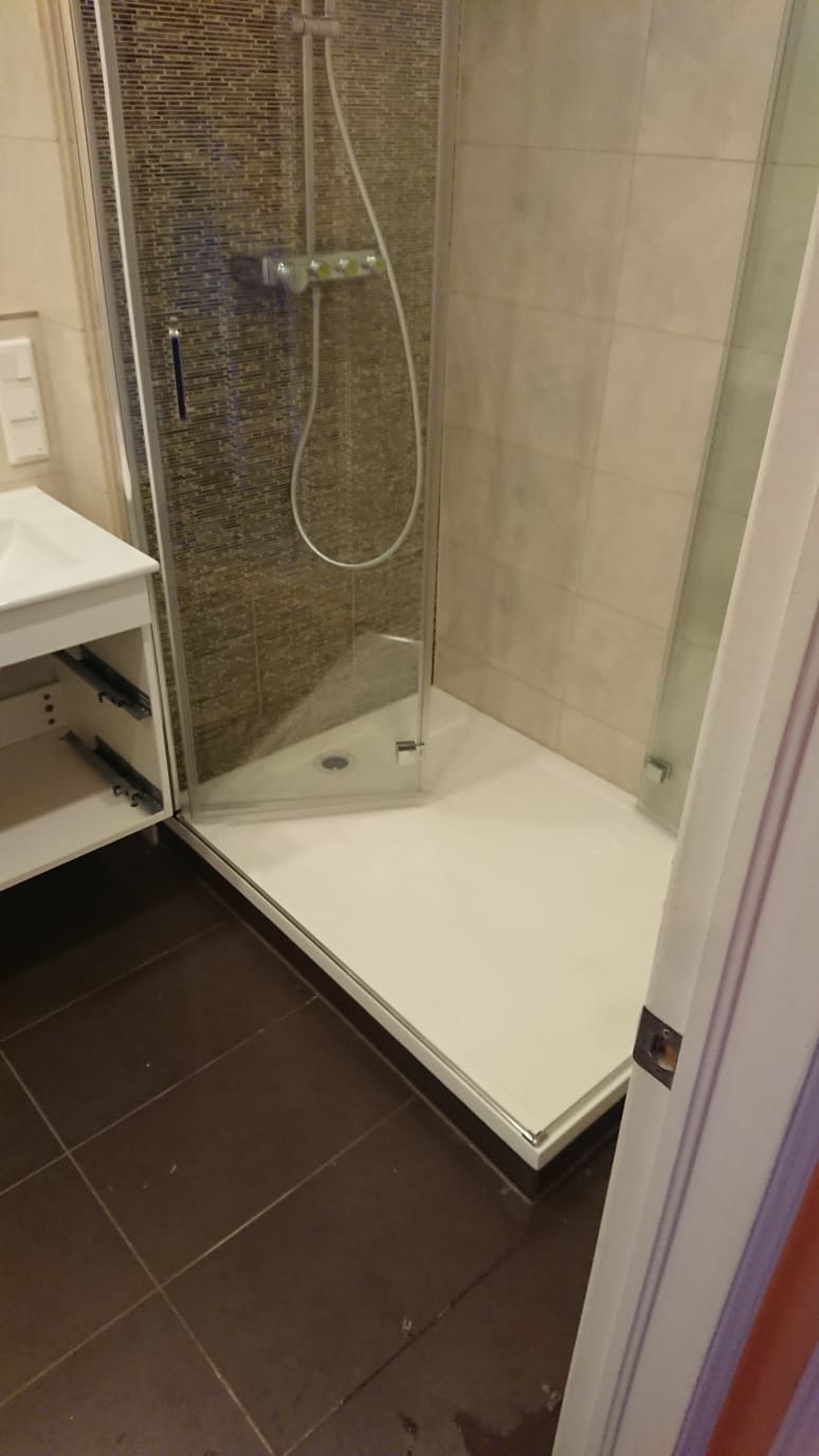 Nowoczesna kabina prysznicowa z brodzikiem, częściowo widoczna szafka umywalkowa z wysuniętymi szufladami, brązowe płytki podłogowe.