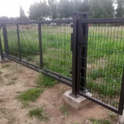 Przesuwna brama panelowa w kolorze antracytowym z widocznym zamkiem, zamontowana na betonowych fundamentach, otoczona trawiastym terenem.