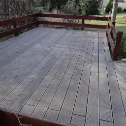 Szara deska tarasowa z drewnianą balustradą, widok z góry na tle zieleni ogrodowej.