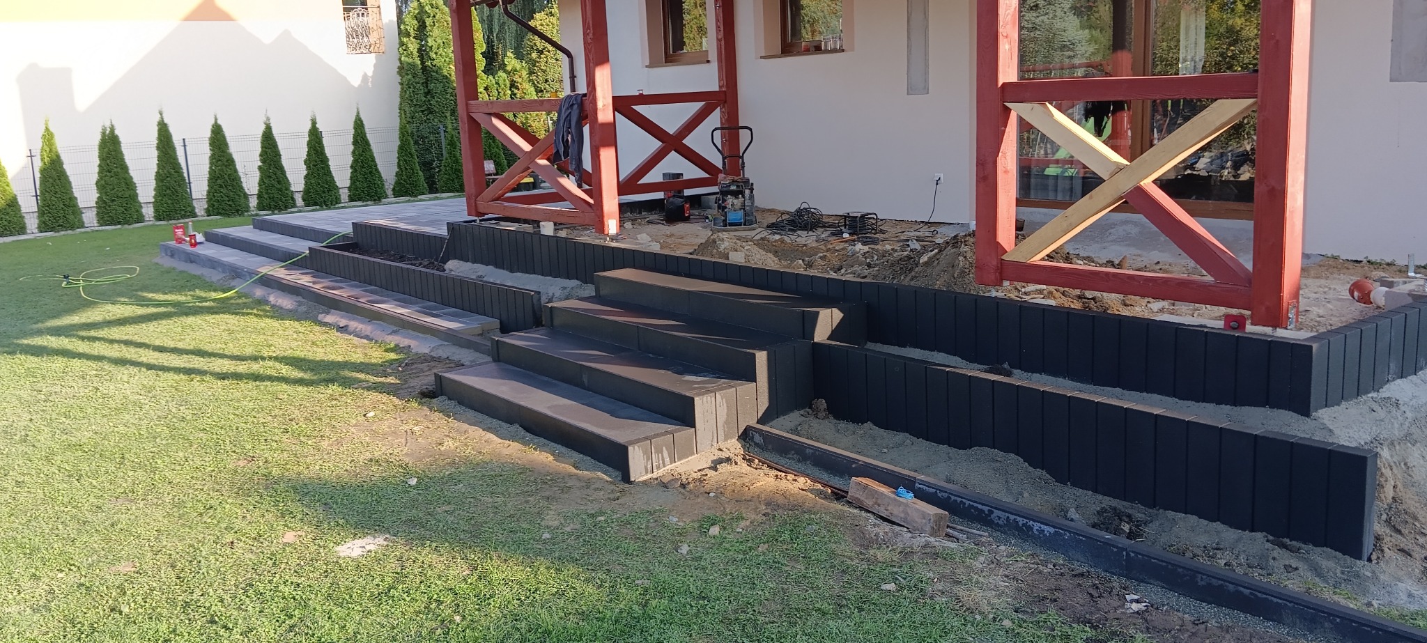 Układanie schodów z kostki brukowej w ogrodzie, widoczne narzędzia i elementy konstrukcyjne, częściowo ukończona realizacja.