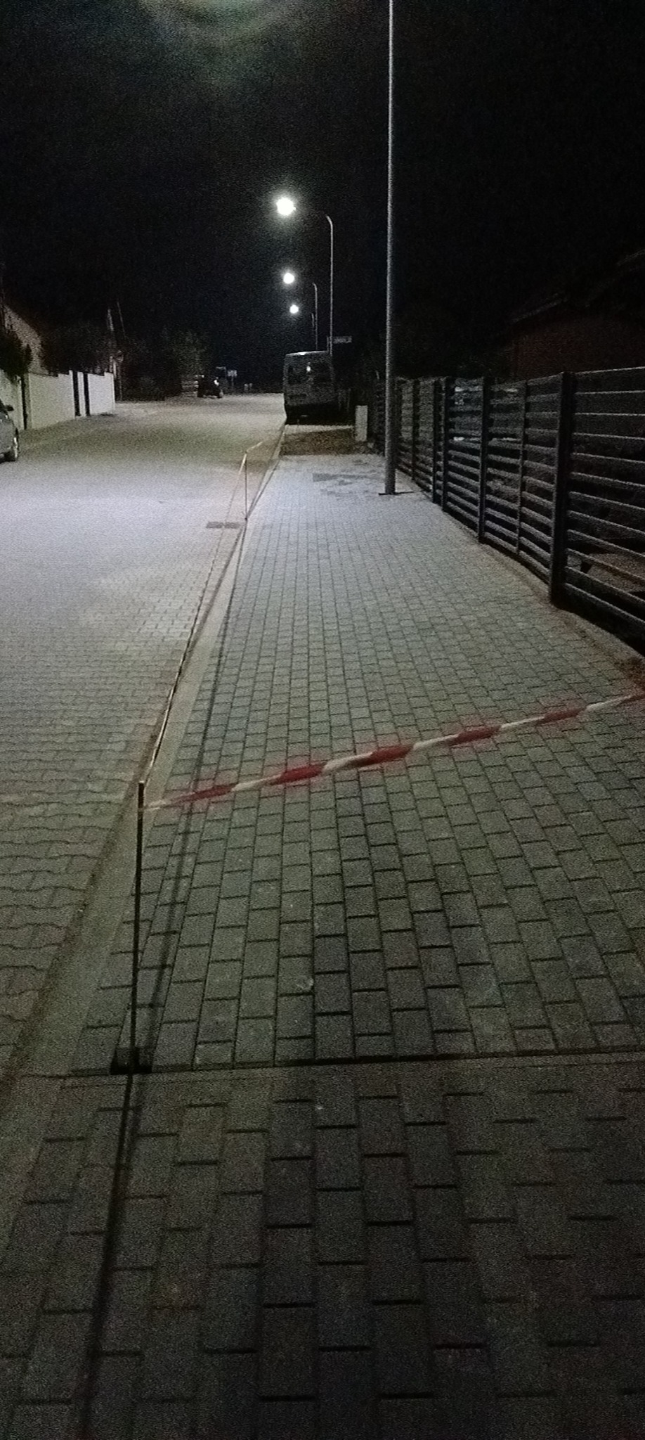 Ułożona kostka brukowa na ulicy w nocy, zabezpieczona taśmą ostrzegawczą, oświetlona latarniami ulicznymi.