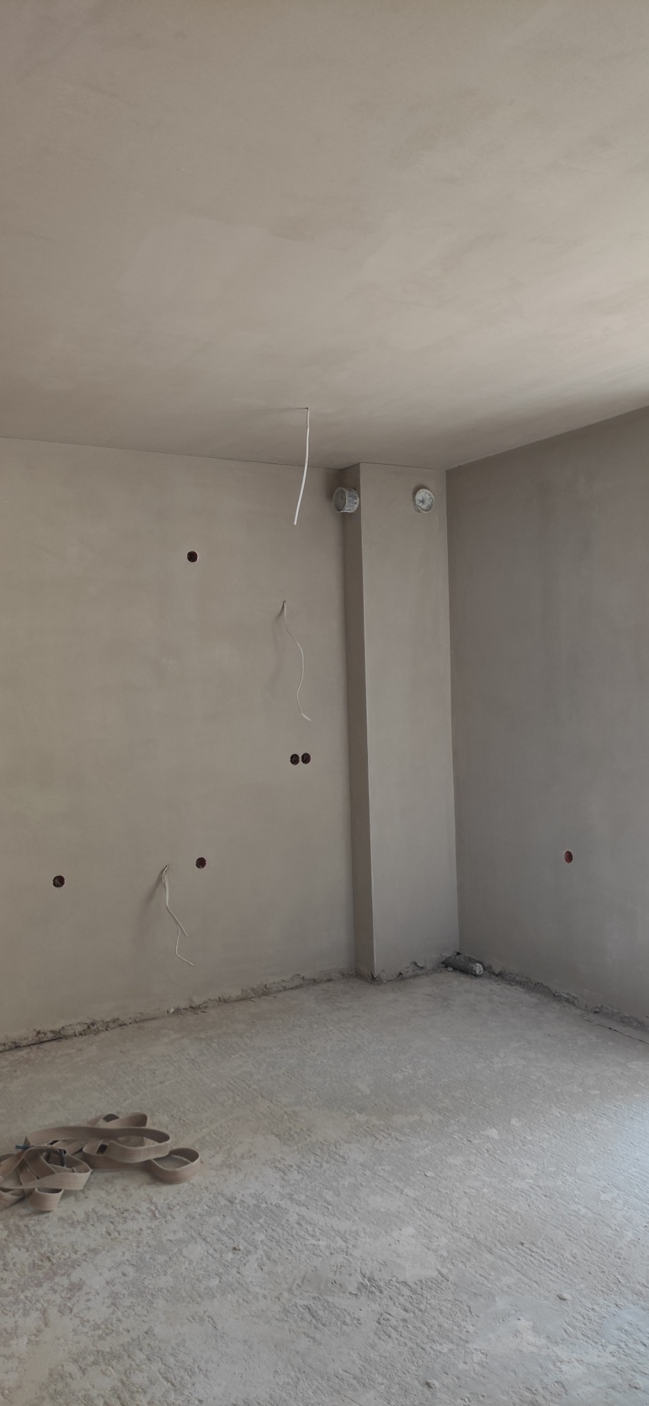 Surowe, otynkowane wnętrze pokoju z wystającymi kablami ze ścian i sufitu oraz taśmą zabezpieczającą na podłodze.