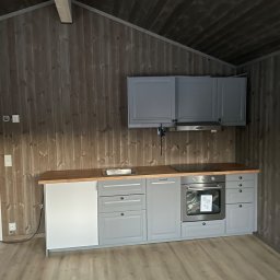 Jakub Parkiety-Malowanie - Szare szafki kuchenne z drewnianym blatem w pomieszczeniu wykończonym drewnem, widoczny fragment podłogi i sufitu.