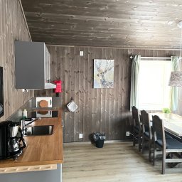 Jakub Parkiety-Malowanie - Wnętrze kuchni w stylu skandynawskim z drewnianymi panelami ściennymi, szarą zabudową kuchenną z drewnianym blatem, stołem z krzesłami i obrazem jelenia na ścianie.