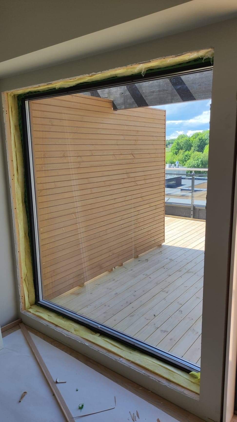 Montaż okna balkonowego z widokiem na taras z desek w Rawa Mazowiecka, widoczna izolacja wokół ramy okiennej.