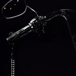 Chromowana kierownica motocykla typu chopper z lusterkiem i czarno-białym frędzlem, sfotografowana w Krakowie na ciemnym tle.